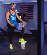 Hombre musculado con martillo y batido en gimnasio ambientado